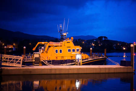 An orange boat with white antennas at the marina at night.South coast of Ireland.の写真素材