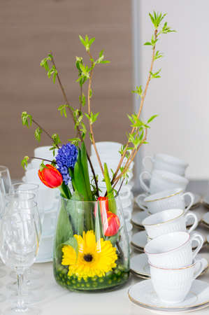 Vase with flowers on a buffet table with wineglasses and white cups. Close up.