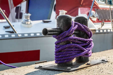 Black bollard with a synthetic rope in a harbor with yacht in a background