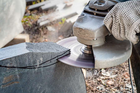 Man's hands holding angle grinder and cutting a stone. Close view.の写真素材
