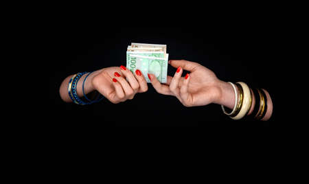 Two women's hands with bracelets pass each other the euro currency. On a black background.の写真素材