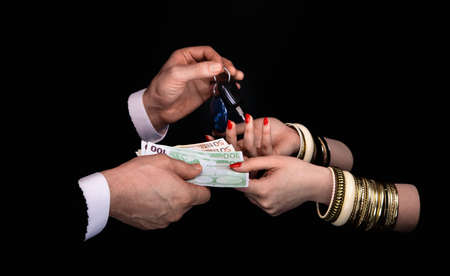 Men's hands giving to  woman's hands euro banknotes and car keys  in a black background