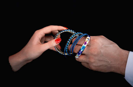 Men's hand giving blue bracelet to woman's hands in a black background