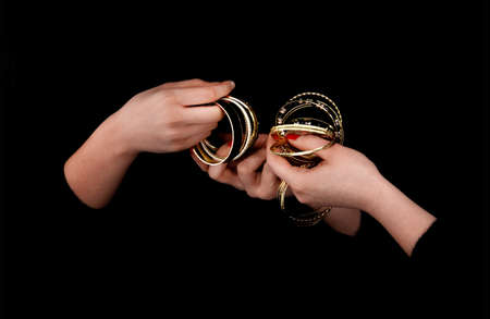 Two caucasian womans hands with golden bracelets on a black background.の写真素材