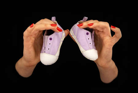 Womanâ€™s hands holding two baby shoes on a black background. Close up.