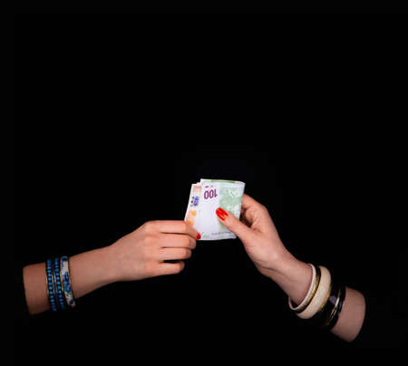 Female's hand giving to other  woman's hand euro banknotes in a black backgroundの写真素材