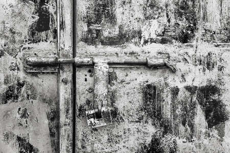 Padlock on a rusty metallic dirty door. Close view. Black white