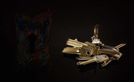 Many similar  metal blank keys  on  the dark background with an old key holeの写真素材