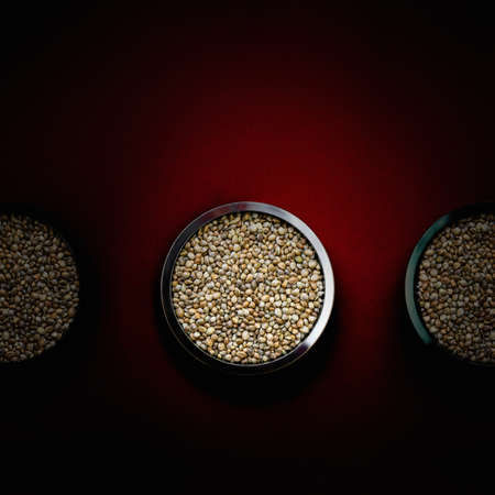 Hemp seeds in metal plates on a dark red background. Close up.の写真素材