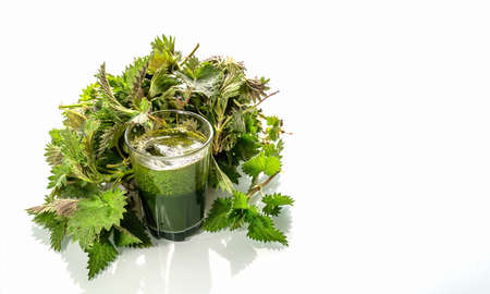 Green raw nettles and a smoothie made of nettles juice in  a glass on a white background. Close...