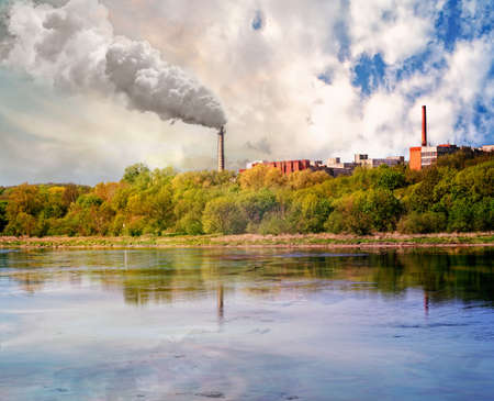 Two chimneys and buildings at the river coast. Smoke from one of them.The concept of ecology.の写真素材