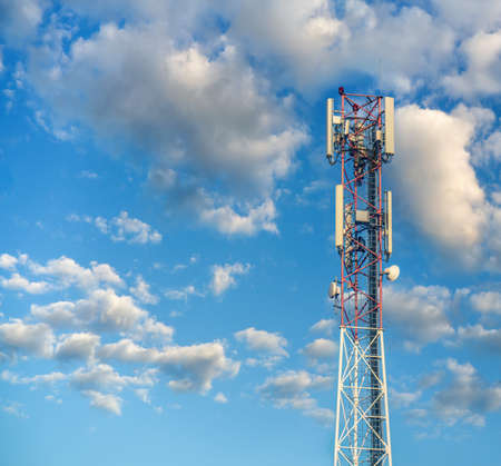 Communication tower with antennas on cloudy sky background.