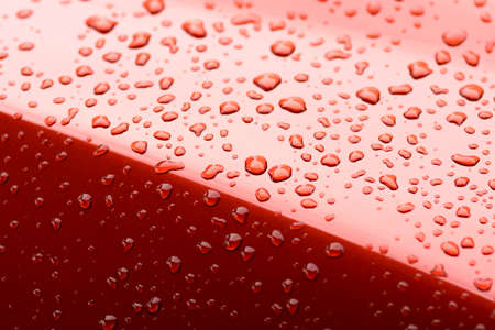 Water drops collect on top of metal red car surfaceの写真素材