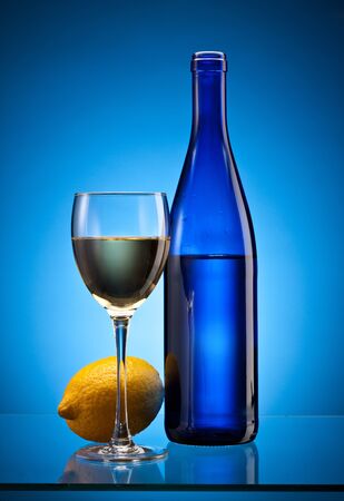 blue bottle with white wine and full glass with lemon over blueの写真素材