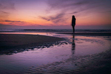Silhouette of a woman walking on the beach at sunset.の写真素材
