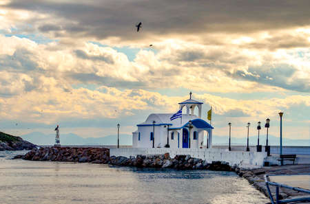 Small chapel with white roofs on cliff over sea and small bay under a dramatic sky on a Greek islandの写真素材