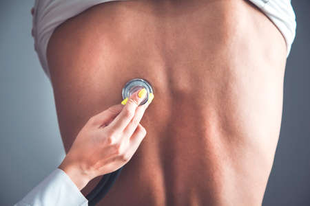 doctor hand stethoscope on ill back on dark backgroundの写真素材