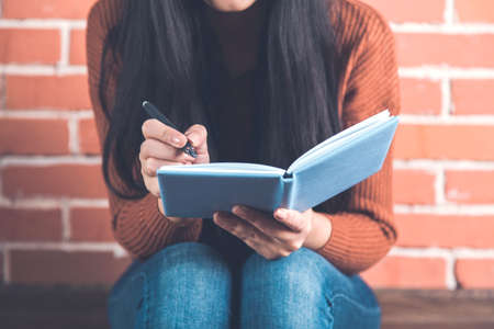 woman hand notepad and pen on brick wall backgroundの写真素材