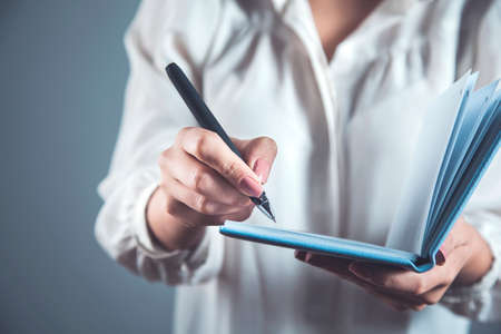 woman hand pen and notepad on gray wall background