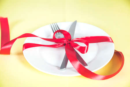 plate with spoon, knife and fork tied with red ribbon on deskの写真素材