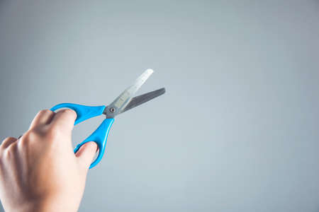 woman hand holding blue scissors on gray background