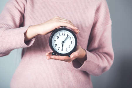 woman hand holding clock on gray background