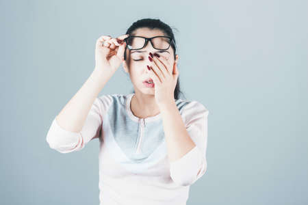 tired young woman eyes glasses on grey backgroundの写真素材