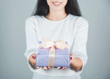 young woman hand holding gift box on grey background