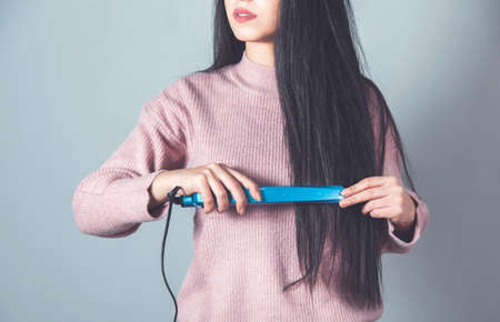 woman iron hair with a hair dryer on gray backgroundの写真素材