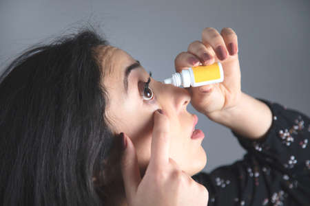 young woman hand eye drops on grey backgroundの写真素材