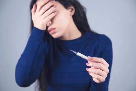 sad ill woman hand thermometer on grey backgroundの写真素材