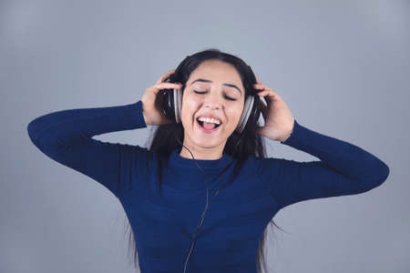 happy young woman ear earphone on grey backgroundの写真素材