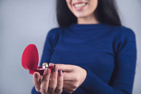 woman hand holding red box with ring on grey background