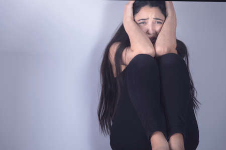 sad woman sitting on ground on the grey background