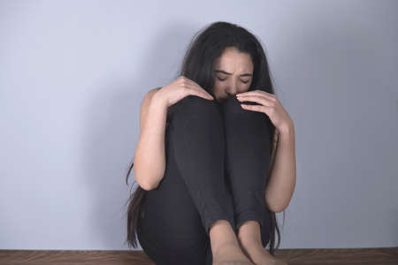 sad woman sitting on ground on the grey backgroundの写真素材