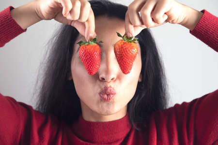 happy woman hand holding strawberries in eyeの写真素材