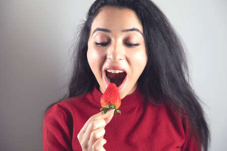 happy woman eat strawberries on grey backgroundの写真素材