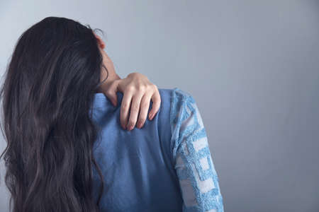 young woman hand in ache shoulder on grey backgroundの写真素材