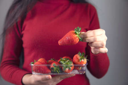 woman hand holding strawberries on red backgroundの写真素材