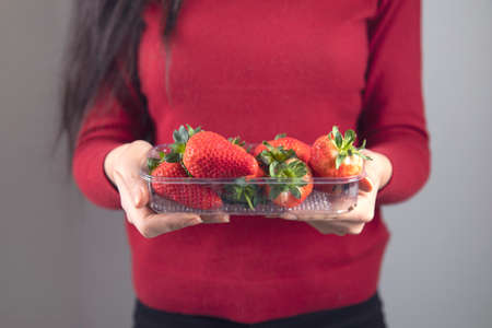 woman hand holding strawberries on red backgroundの写真素材