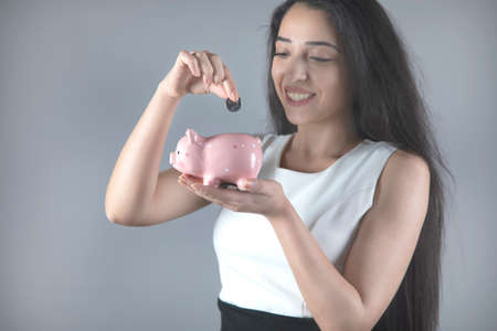 business woman hand coin and piggy bank on grey backgroundの写真素材