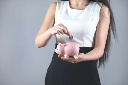 business woman hand coin and piggy bank on grey backgroundの写真素材