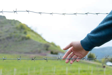 man hand and barbed wire in landscape background