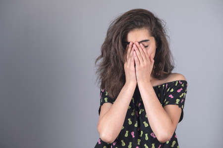 sad woman hand in face on gray background