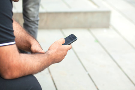 man using a smart phone sitting in street