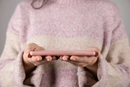 woman hand holding pink phone on gray background