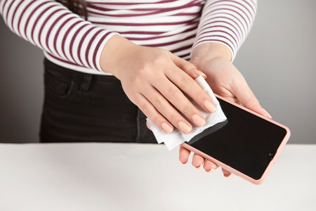 Woman cleaning mobile phone with antiseptic wipeの写真素材