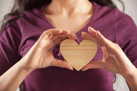 Young woman holding wooden heart sign.