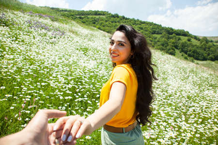happy woman and man hand in hand in the chamomile fieldの写真素材