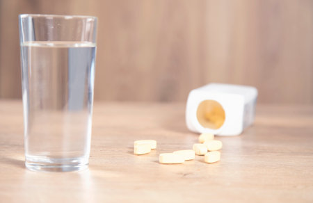 yellow drugs with glass of water on tableの写真素材